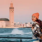 Smiling traveler in front of Hassan II Mosque in Casablanca at the start of a 10-day Casablanca to Sahara tour in Morocco
