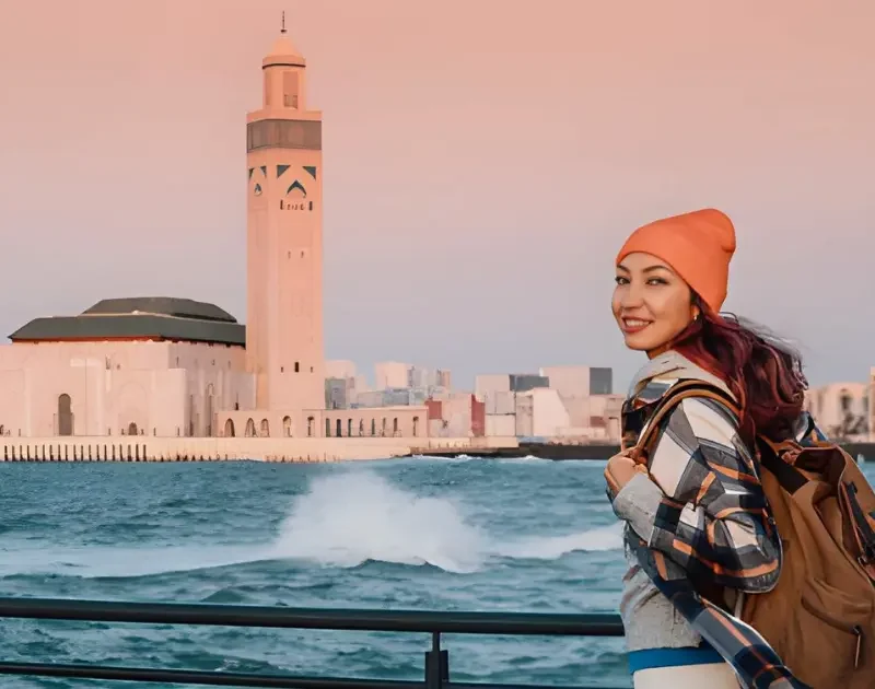 Smiling traveler in front of Hassan II Mosque in Casablanca at the start of a 10-day Casablanca to Sahara tour in Morocco