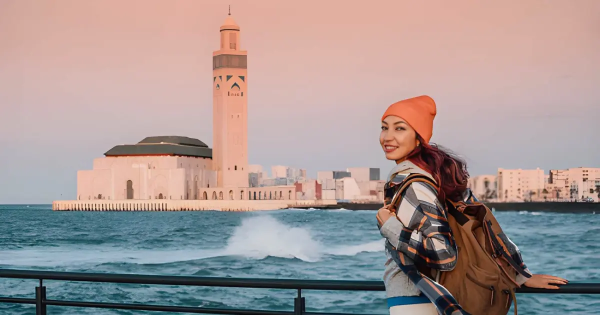 Smiling traveler in front of Hassan II Mosque in Casablanca at the start of a 10-day Casablanca to Sahara tour in Morocco
