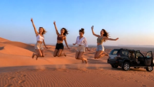 Group of friends enjoying a girls' trip in the Sahara Desert, Morocco, beside a 4x4 vehicle.